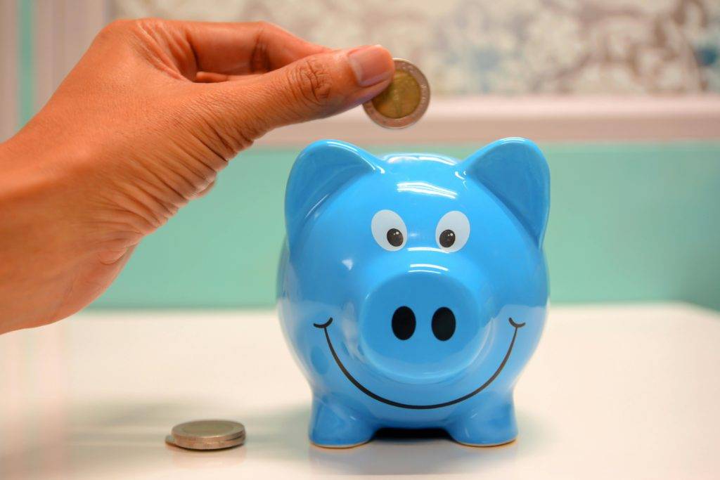 A hand putting a coin into a blue piggybank