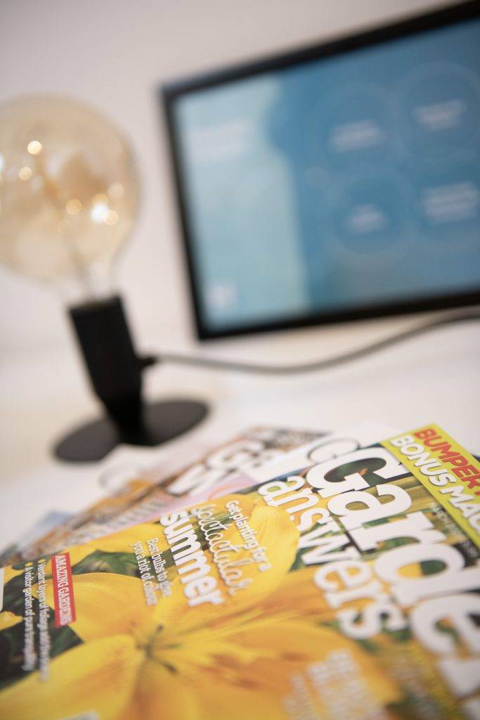 Two gardening magazines on a PR agency desk with a lamp and photo frame in the background